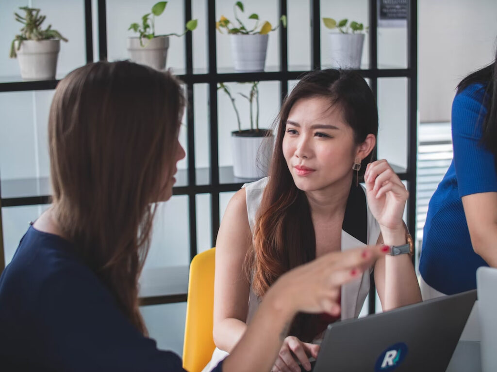 a woman in white listening to another person explaining something