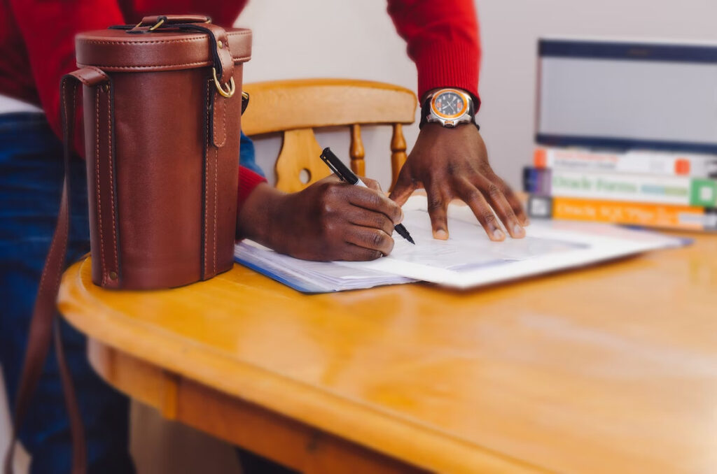 a man writing something on a paper beside a unique brown leather sling bag