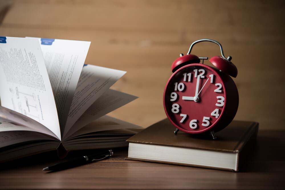 an image showing a clock with a book and a pen on the table