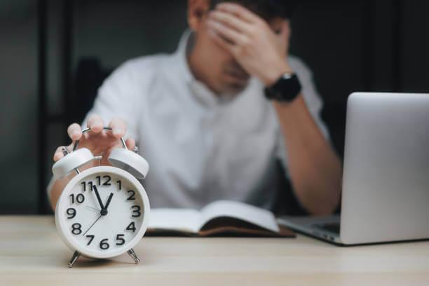 a person holding an alarm clock while cupping his forehead
