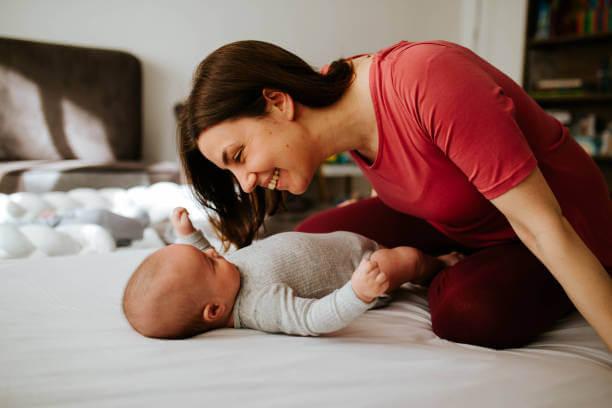 a woman playing with a baby on the bed